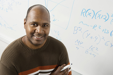 African-American man at a classroom board with equations on it.
