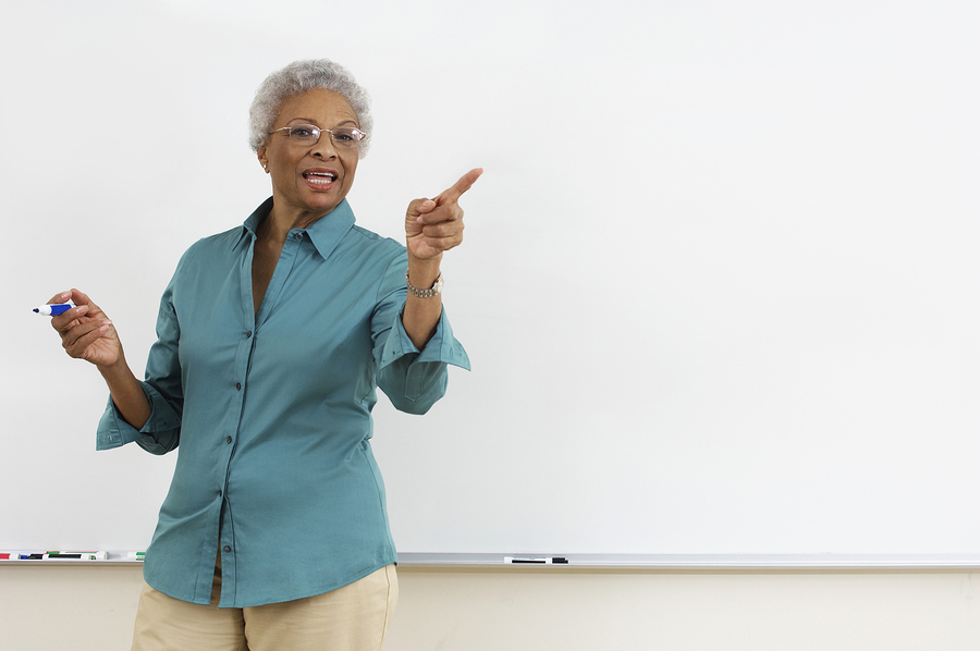 African-American female instructor at board pointing to off-camera students